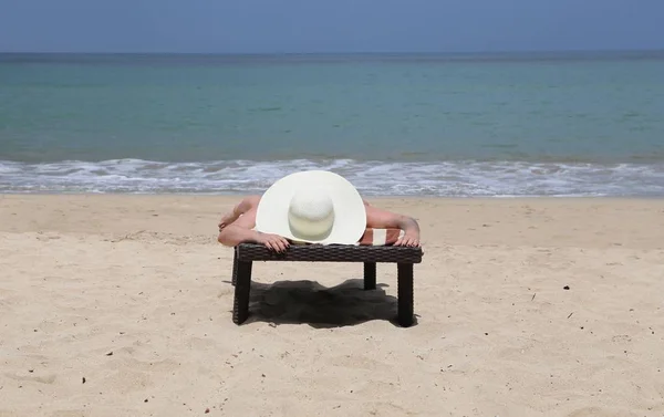 Figure of a man on a bed on the sea shore in a white straw hat sunbathing in the sun