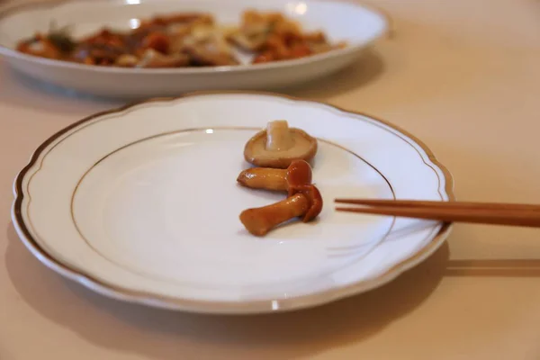 Mushrooms are small salty in sauce wet on a plate of white and sticks for eating