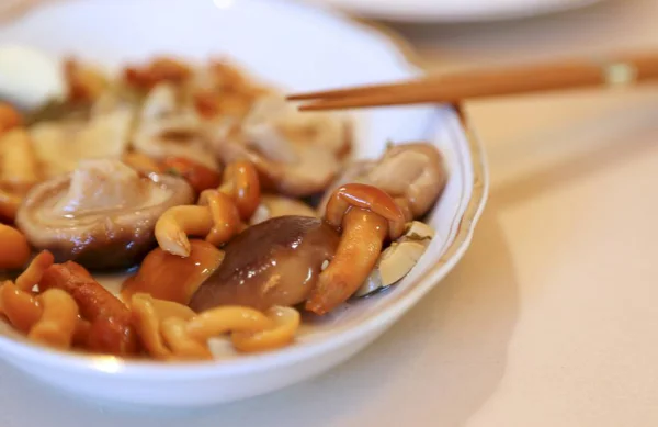 Mushrooms are small salty in sauce wet on a plate of white and sticks for eating