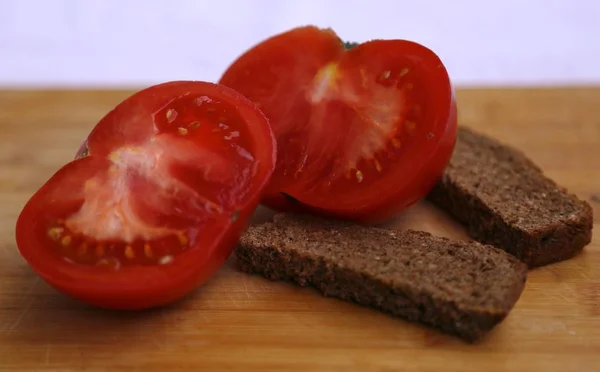 Two pieces of black bread and a tomato cut into two pieces