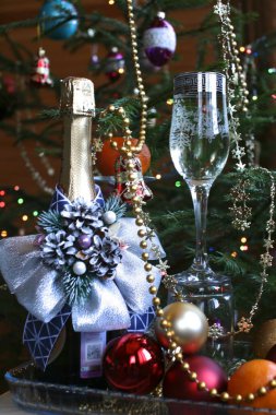 Kapalı şarap şişesi parlak mavi bir banyo ve şarapla süslenmiş arkaplanda Noel ağacı ve Noel ağacı süslemeleri var.