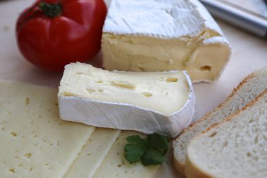 Parça parça kesilmiş beyaz ekmek, büyük parçalarla kesilmiş peynir ve yanında da domates ve peynir bıçağı.