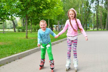 Oğlan ve kız el ele tutuşup parkta paten kayıyorlar.