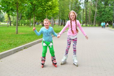 Kız, küçük kardeşine parkta paten kaymayı öğretiyor.