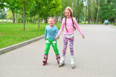 Kız küçük oğlana parkta paten kaymayı öğretiyor.