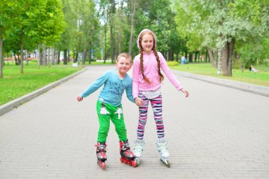 Kız, küçük erkek kardeşinin parkta paten kaymasına yardım ediyor.