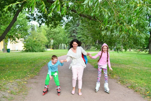 Mujer apoya la mano de los niños sonrientes en patines en Imagen De Stock