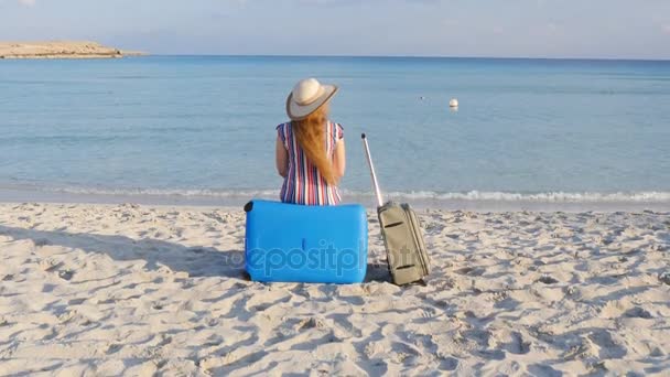 Молодая женщина-путешественница сидит на пляже с чемоданом — стоковое видео