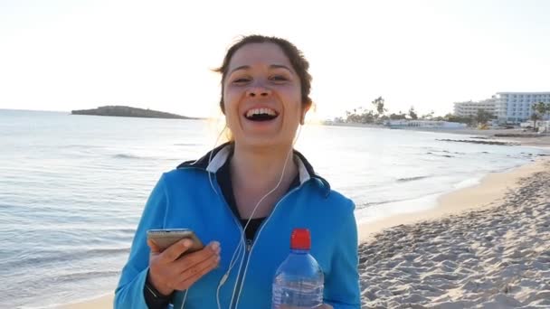 Glimlachend vrouwelijke Jogger bij zonsondergang op het strand — Stockvideo