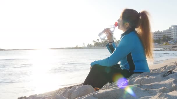 Fiatal nő a sport ruházat iszik víz edzés után a strandon — Stock videók