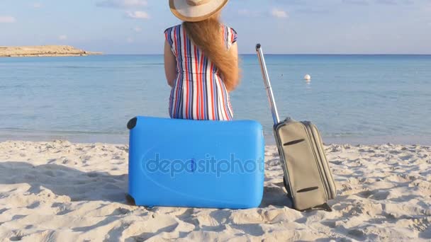 Mladá žena s kufrem sedí na pláži — Stock video