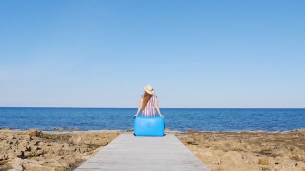 Reisende Frau sitzt auf ihrem Koffer am Strand — Stockvideo