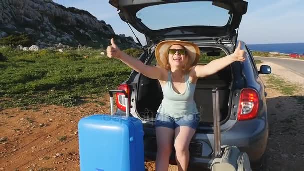 젊은 여자는 자동차의 트렁크에 앉아 있다. 여행 컨셉 — 비디오