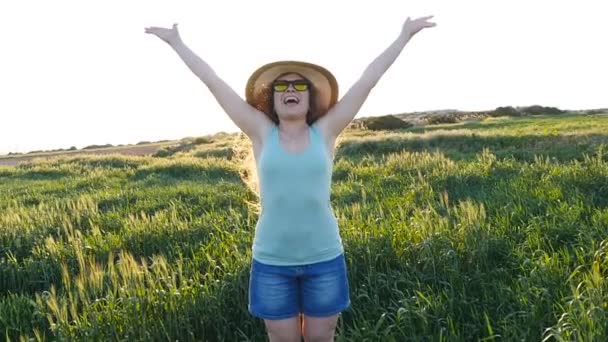 Jovem feliz de chapéu desfrutando de verão no campo verde ao pôr do sol — Vídeo de Stock