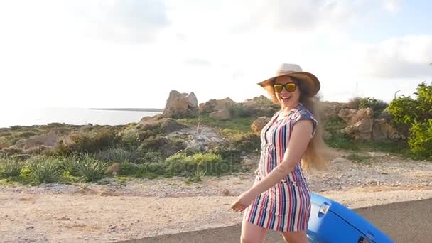Νεαρή γυναίκα ταξιδιώτης σε ένα καπέλο που τρέχει με μια μπλε βαλίτσα — Αρχείο Βίντεο