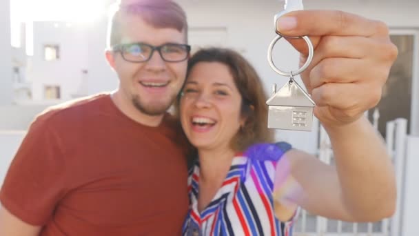 Happy νεαρό ζευγάρι που στέκεται κρατώντας σε εξωτερικούς χώρους το κλειδί στο νέο σπίτι τους — Αρχείο Βίντεο