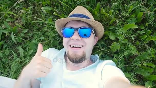 Homem feliz está deitado em uma grama em um parque tirando selfie — Vídeo de Stock