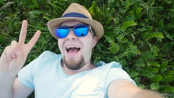 El hombre feliz está tumbado en un césped en un parque tomando selfie — Vídeos de Stock