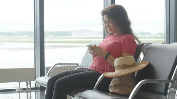 Une jeune femme à l'aéroport attend le départ et regarde le smartphone — Video