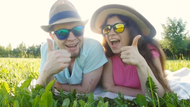 Молодая пара лежит в траве и улыбается — стоковое видео