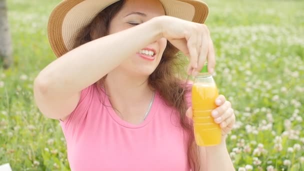 Молода жінка п'є сік в парку — стокове відео