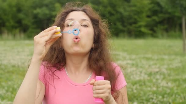 Mladá žena fouká mýdlové bubliny v parku — Stock video