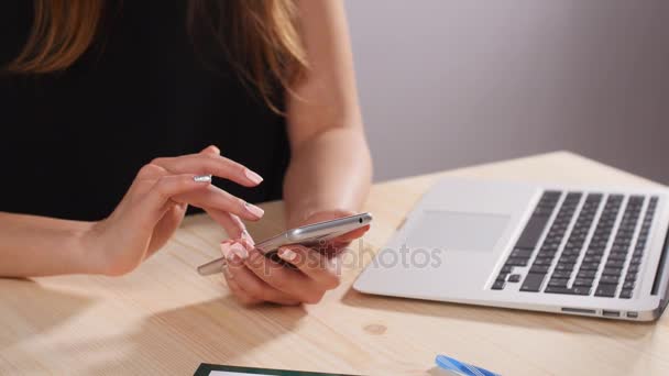 Uma menina está trabalhando no escritório atrás de um computador com um smartphone — Vídeo de Stock