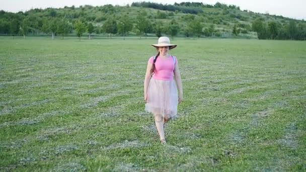 Una joven con sombrero camina por el campo verde — Vídeos de Stock