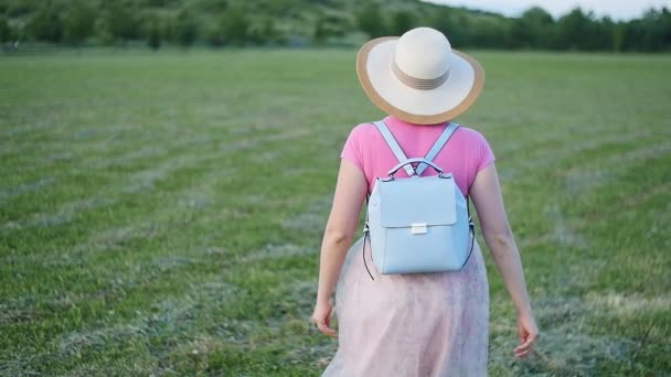 Una joven con sombrero camina por el campo verde — Vídeos de Stock