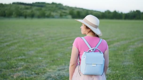 Uma jovem de chapéu caminha pelo campo verde — Vídeo de Stock