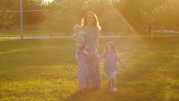 Μια νεαρή μητέρα είναι το περπάτημα στο πάρκο στο ηλιοβασίλεμα — Αρχείο Βίντεο