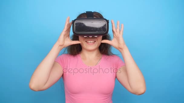 Ευτυχισμένη γυναίκα χρησιμοποιώντας μια κάσκα εικονικής πραγματικότητας σε μπλε φόντο — Αρχείο Βίντεο
