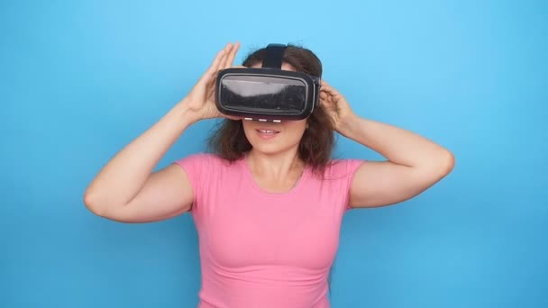 Šťastná mladá žena pomocí soupravu pro virtuální realitu na modrém pozadí — Stock video