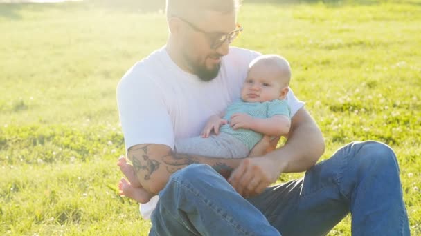 Père et fils assis ensemble sur l'herbe au coucher du soleil d'été soir — Video