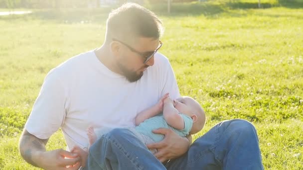Otec a syn spolu seděli na trávě v létě večerní slunce — Stock video