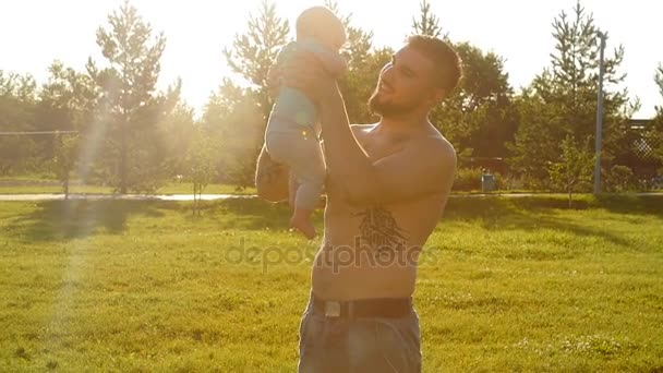 Pai segura bebê filho em seus braços ao pôr do sol — Vídeo de Stock