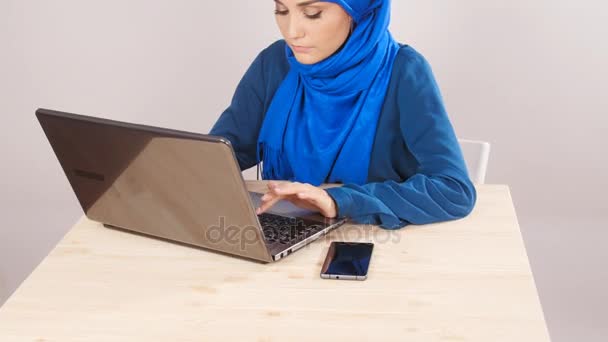 Молодая мусульманка, сидящая в офисе и работающая на ноутбуке — стоковое видео
