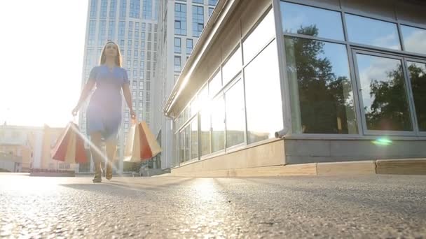 Ung kvinna med shoppingkassar promenerar längs gatan — Stockvideo