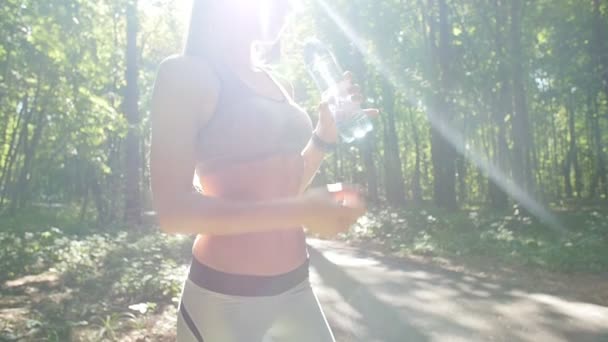 Молодая спортсменка пьет воду после пробежки на закате в летнем лесу — стоковое видео
