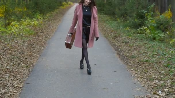 Молодая женщина с чемоданом в осеннем парке — стоковое видео
