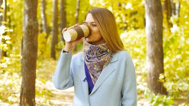 Carina giovane donna con una tazza di caffè nel parco autunnale — Video Stock