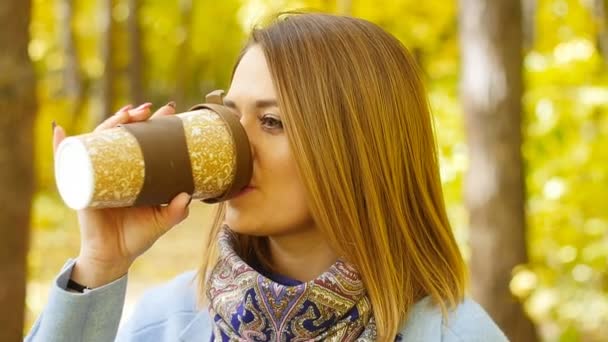 Nette junge Frau mit einer Tasse Kaffee im Herbstpark — Stockvideo
