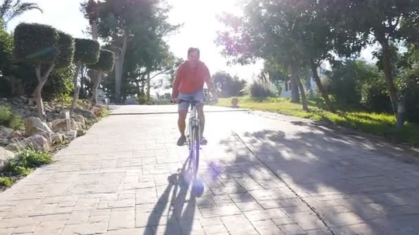 Joven en bicicleta en la ciudad al atardecer en verano — Vídeo de stock