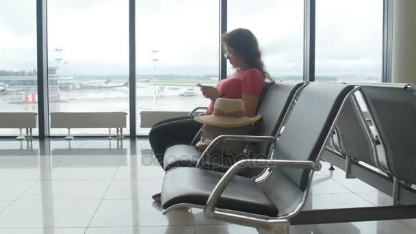 Jovem passageira no aeroporto, usando seu telefone enquanto espera por seu voo — Vídeo de Stock