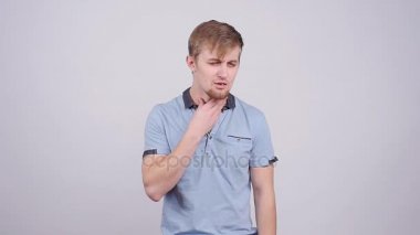 Boynuna dokunuyor ve gri arka plan üzerinde boğaz ağrısı acı mutsuz genç adam