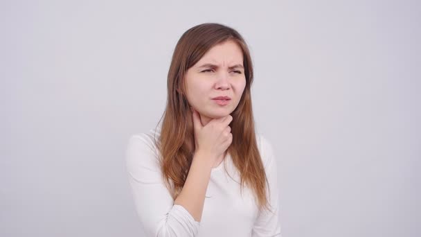 Uma jovem mulher tem uma dor de garganta em um fundo cinza — Vídeo de Stock