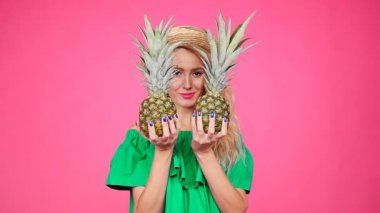 Bir iki ananas pembe bir arka plan üzerinde tutan mutlu genç sarışın kadın