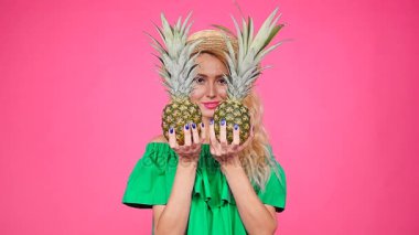 Bir iki ananas pembe bir arka plan üzerinde tutan mutlu genç sarışın kadın