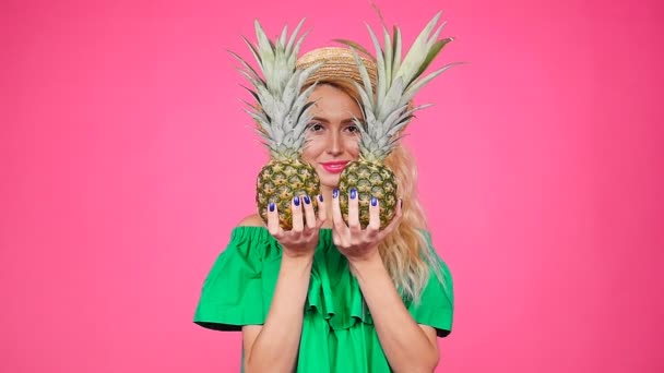 Happy young blonde woman holding a two pineapple on a pink background — Stock Video