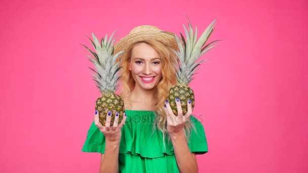 Happy young blonde woman holding a two pineapple on a pink background — Stock Video